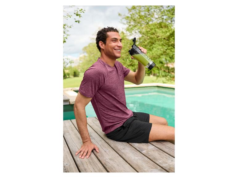 Een man in een CRIVIT functioneel shirt zit bij het zwembad en drinkt een groene shake.