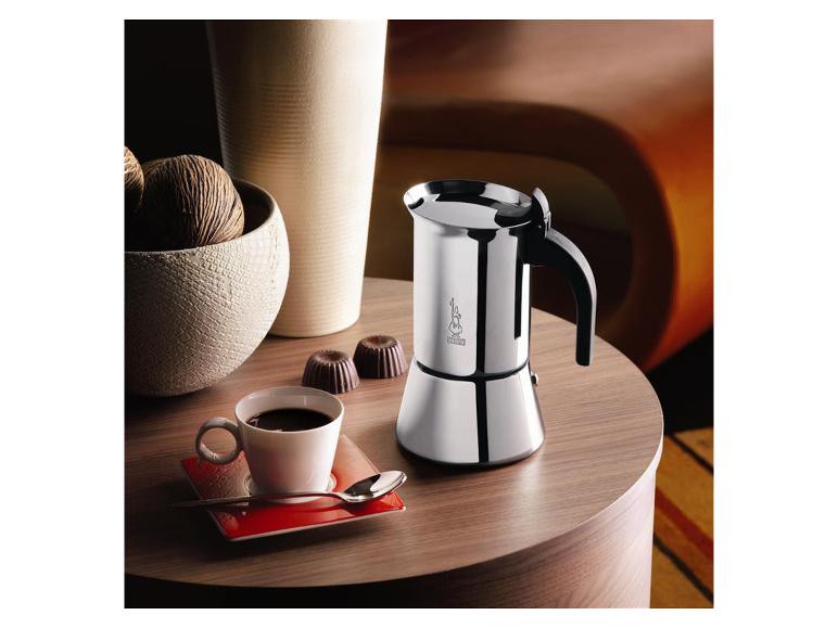 Zilveren mokkapot, kopje koffie en chocoladebonbons op een houten tafel.