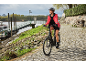 Vrouw op een elektrische fiets op een kasseiweg langs de rivier.