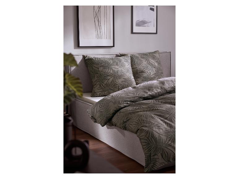 Bed met grijs beddengoed met bladpatroon en twee ingelijste kunstwerken aan de muur.