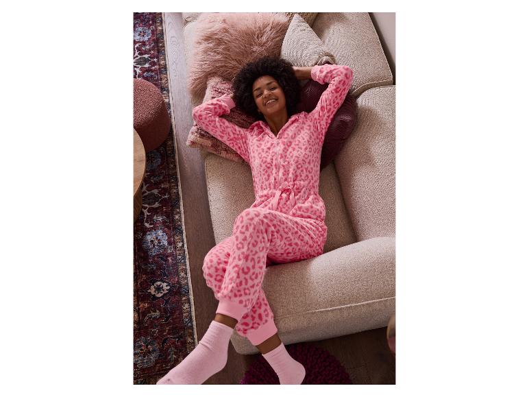 Vrouw in een roze luipaardprint onesie, liggend op een beige bank.