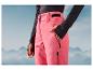 Een vrouw draagt roze ski-broek tegen een achtergrond van bergen.