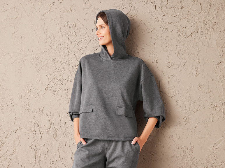 Een vrouw draagt een grijze hoodie en broek