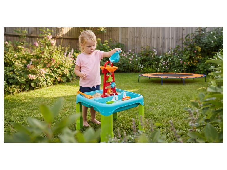 Meisje speelt met water-zandtafel met molen en bootjes in de tuin.