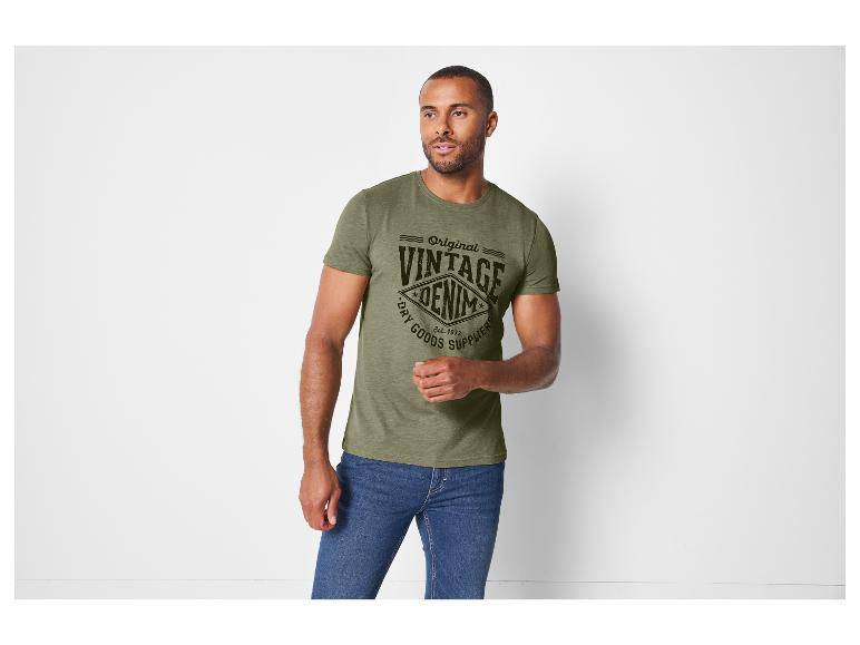 Man draagt een groene T-shirt met 'Vintage Denim' print en blauwe jeans.