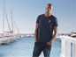 Man in een donkerblauw T-shirt met een 'Royal Navy'-logo, in een jachthaven.