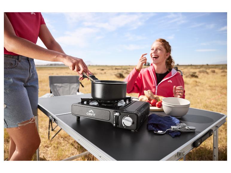 Vrouw kookt op draagbaar gasfornuis, terwijl andere vrouw lacht op de achtergrond.