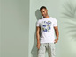 Man draagt een witte T-shirt met een print van 'Paradise' en een groene broek.
