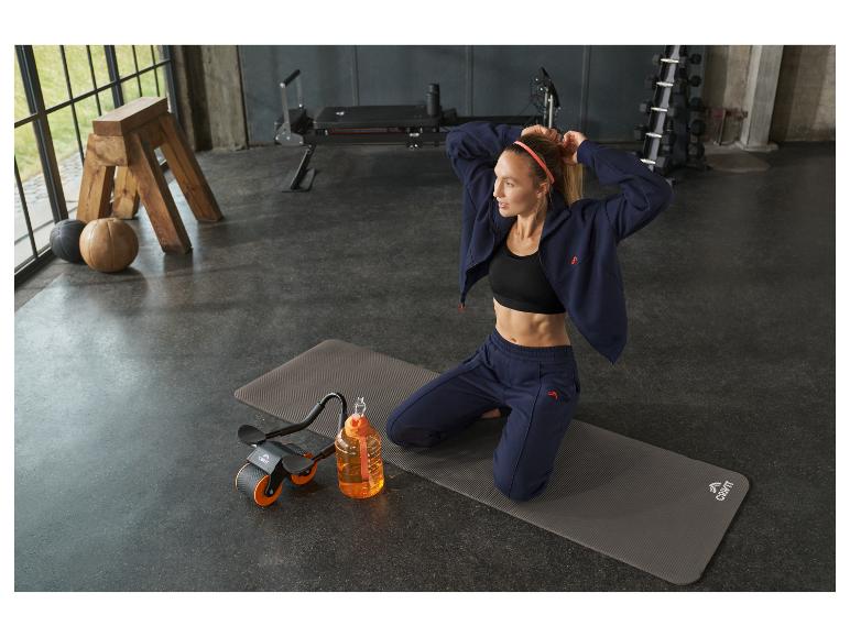 Vrouw in sportkleding op yogamat met waterfles en trainingsapparatuur.