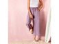 Vrouw in paarse broek en witte slippers, leunend tegen een surfboard.