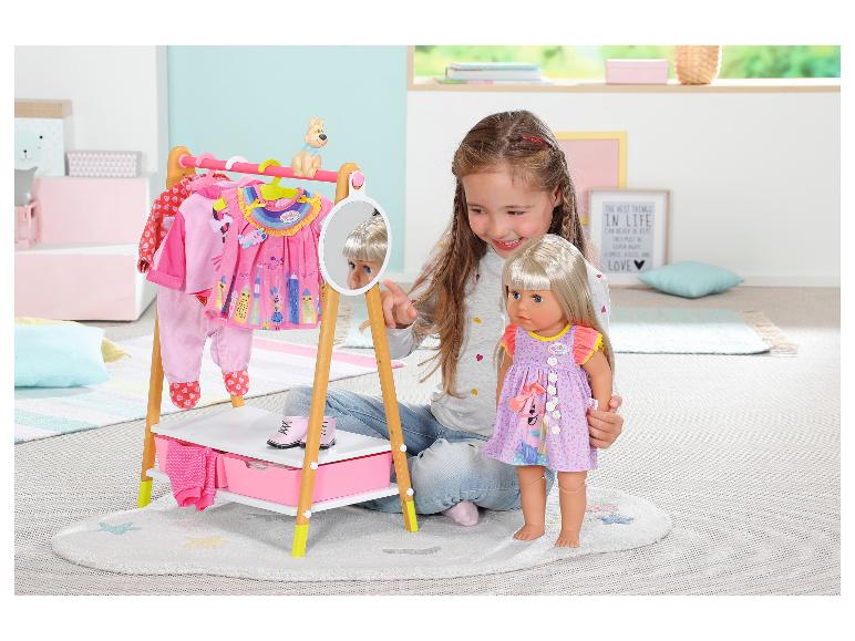 Meisje speelt met BABY born pop en kledingrek met poppenkleding.