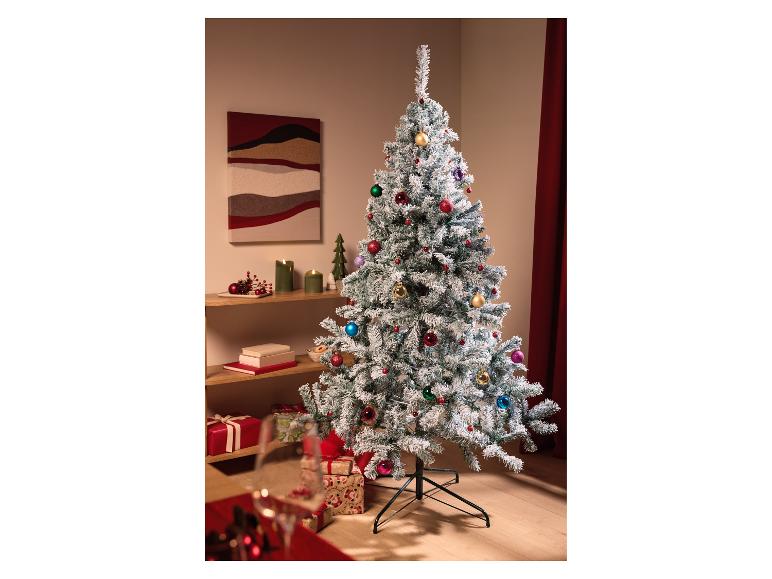 Een bevlokte kerstboom met kleurrijke ornamenten in een feestelijke woonkamer.