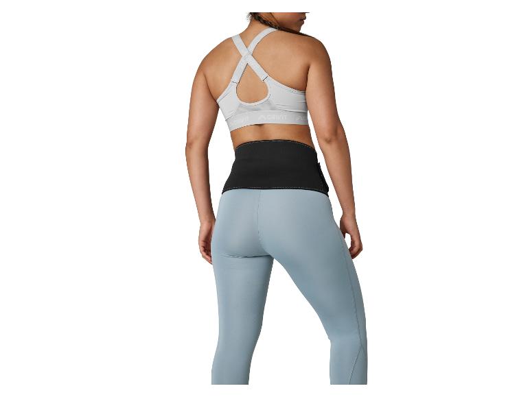 Vrouw in grijze sportbeha, zwarte fitnessriem en blauwe legging, achteraanzicht.
