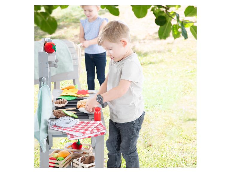 Kinderen spelen buiten met een speelgoedbarbecue en vilten eten.