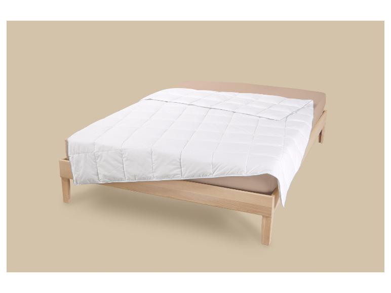 Wit dekbed op een houten bed met een beige hoeslaken.