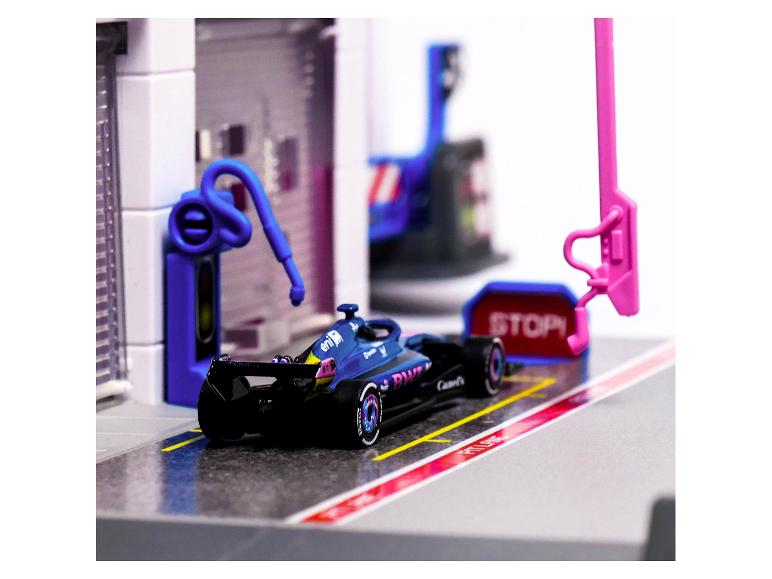 Blauwe raceauto in een pitstop met een 'STOP'-bord en tankapparatuur.