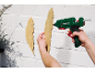 Een persoon gebruikt een Parkside lijmpistool om een decoratieve veer aan een muur te bevestigen.
