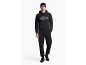 Man in zwart trainingspak met hoodie en muts.