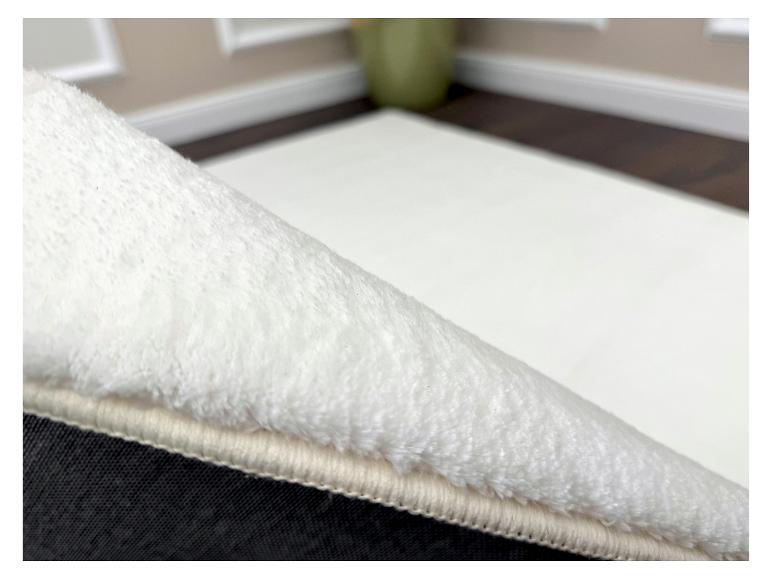 Wit pluizig tapijt met antislip onderkant, liggend op een houten vloer.