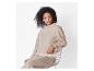 Vrouw in een beige coltrui en bijpassende broek, zittend op een draadstoel.