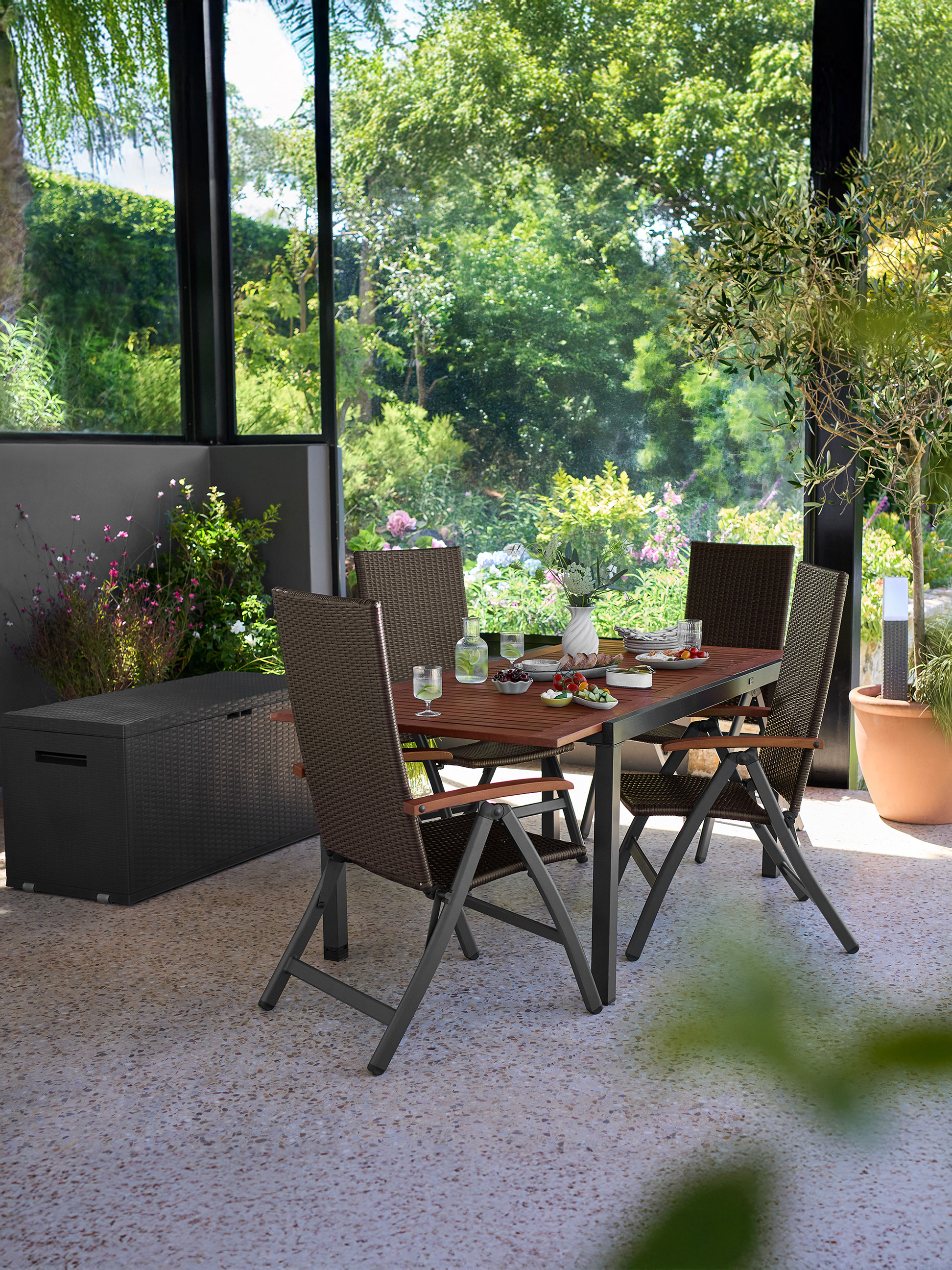 Terras-eetset met bruine stoelen en houten tafel, omringd door groen.