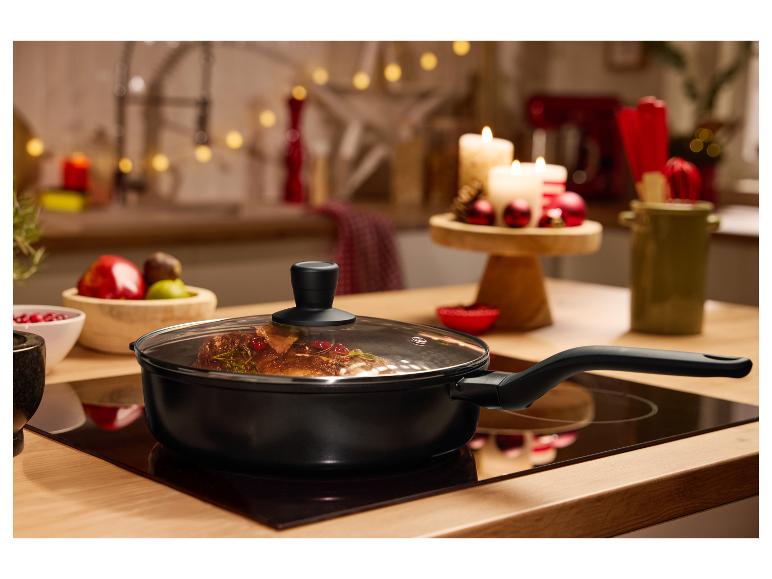 Zwarte koekenpan met glazen deksel op een kookplaat, met feestelijke decoratie op de achtergrond.