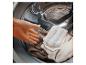 Een hand legt kleding en een mop in een wasmachine.