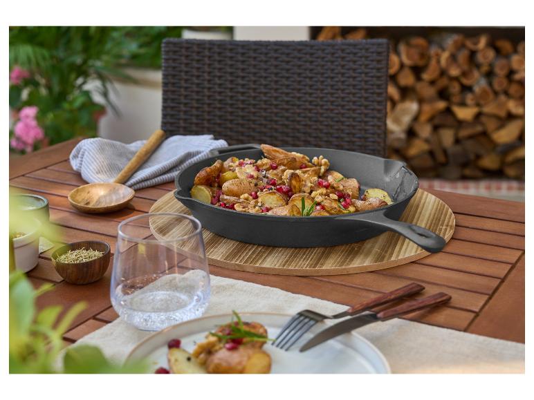 Gietijzeren pan met aardappelen, granaatappel en walnoten op een houten buitentafel.