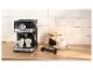 Zwart espressomachine met twee kopjes, gemalen koffie en een kop cappuccino op een houten aanrecht.