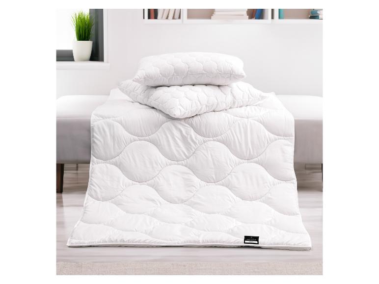 Wit dekbed en kussens met een golvend patroon op een bed in een lichte kamer.