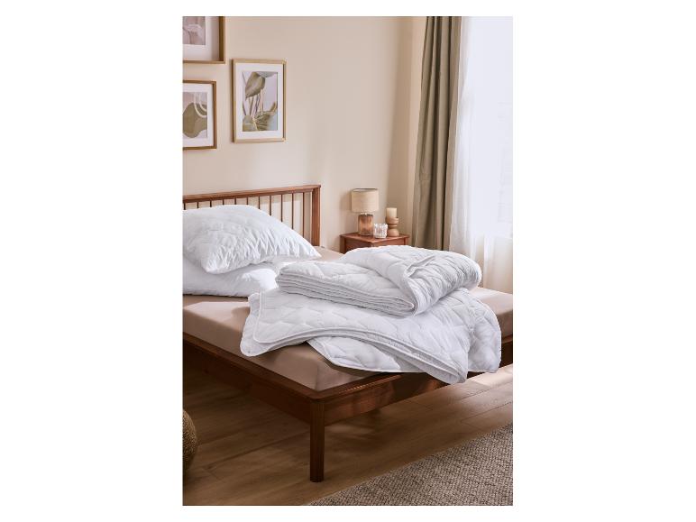 Witte gewatteerde kussens en dekbed op een houten bed in een gezellige slaapkamer.