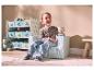 Jongen zit in kinderfauteuil met houten trein, opbergrek op de achtergrond.