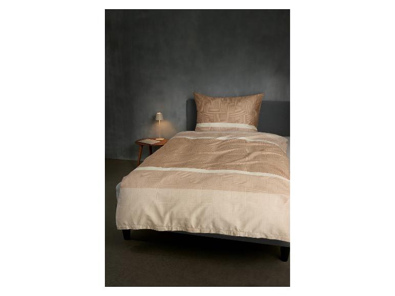 Beige beddengoed met geometrisch patroon op bed in slaapkamer met nachtlampje.