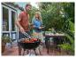 Man grilt steaks en tomaten, vrouw brengt brood buiten in de tuin.