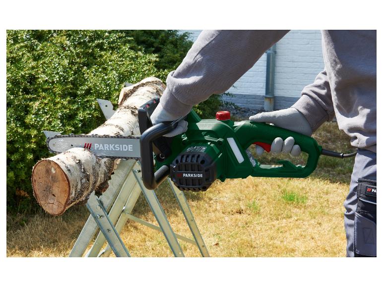 Persoon zaagt een boomstam met een groene Parkside elektrische kettingzaag op een zaagbok.