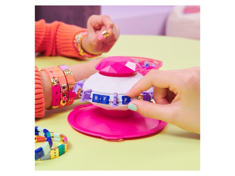 Een roze armband-maker met kralen en een stapel kleurrijke armbanden.