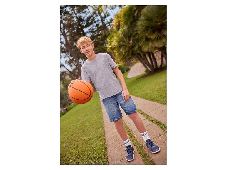Jongen in grijs T-shirt, spijkerbroek en sneakers met een basketbal op een pad.