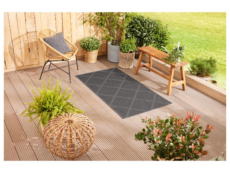 Een grijs outdoor vloerkleed op een houten terras met een wicker stoel en planten.