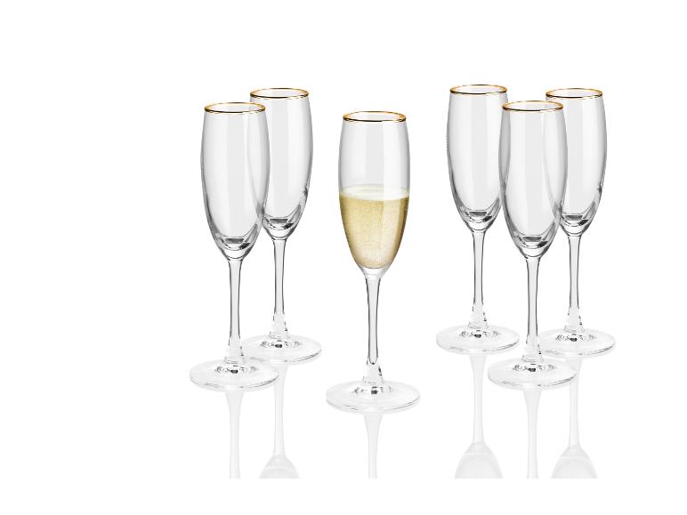 Een set champagne glazen met een gouden rand, waarvan één gevuld is.