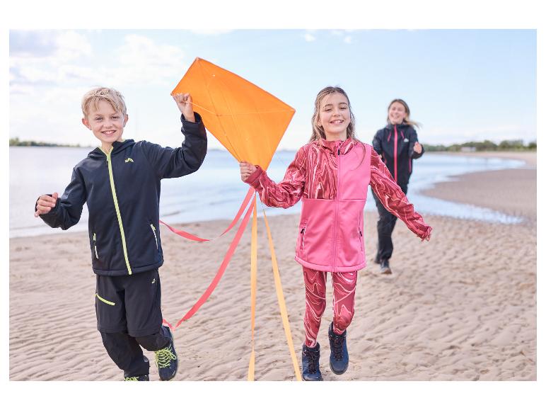 Kinderen in CRIVIT softshelljassen rennen op het strand met een vlieger.