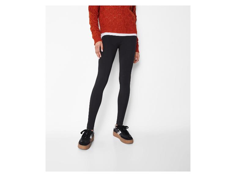 Zwarte dameslegging met een oranje trui en zwarte sneakers.
