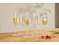 Zes champagneglazen, sommige gevuld met mousserende wijn, en drie frambozen op een houten tafel.
