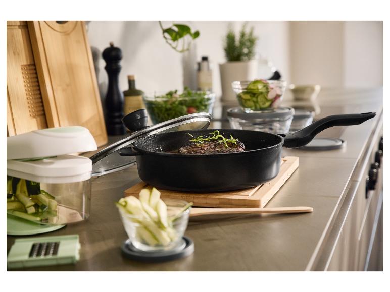 Een zwarte pan met een biefstuk en kruiden, omringd door keukengerei.