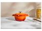 Oranje gietijzeren pan op een wit marmeren oppervlak met een pot pasta en een houten lepel.
