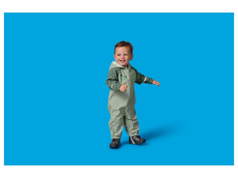 Peuter in een groen regenpak met dinosaurusprint, lachend en staand.