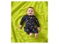Een lachende baby in sterren- en maanpyjama, liggend op een groene deken.