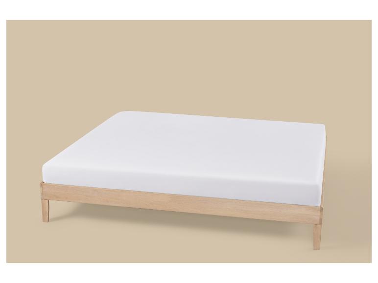 Wit matras op een licht houten bedframe tegen een beige achtergrond.