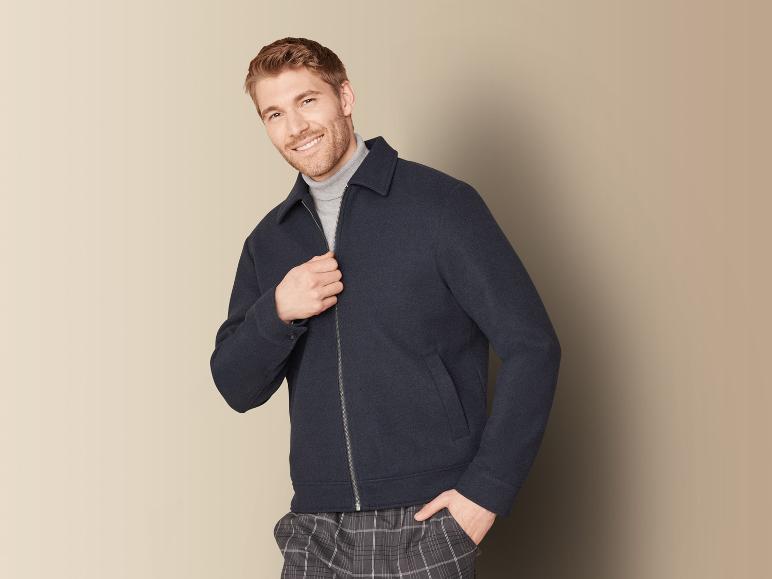 Een man draagt een donkerblauwe jas met rits en een geruite broek.