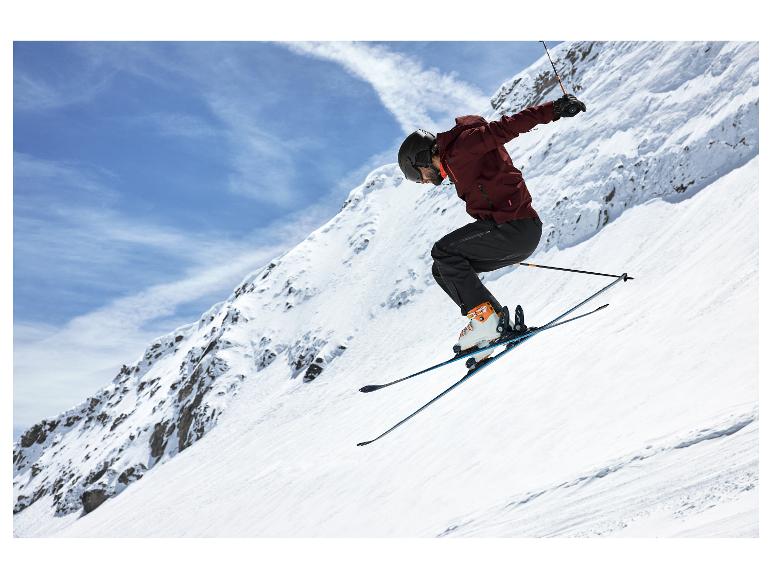Een skiër in ski-jack en -broek, met helm en bril, springt op een besneeuwde helling.
