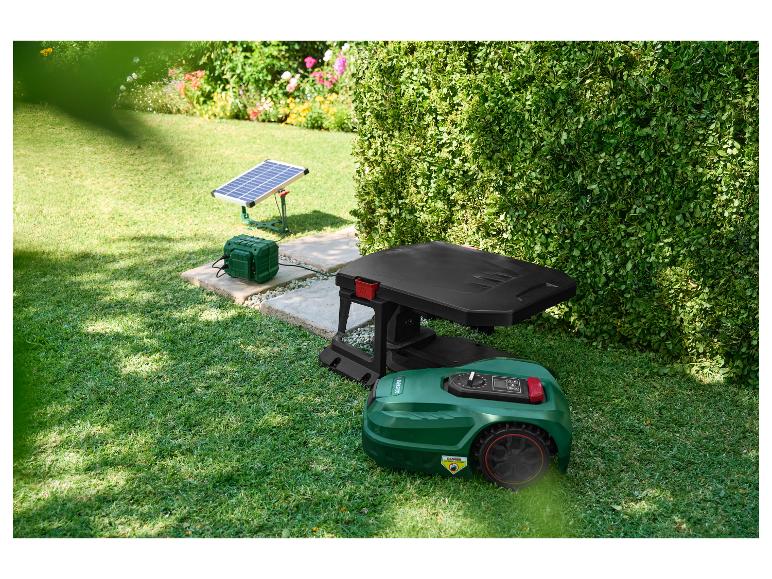 Robotmaaier met laadstation en zonnepaneel in een tuin.